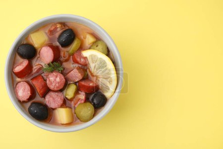 Téléchargez les photos : Soupe de viande solyanka avec de fines saucisses fumées sèches dans un bol sur fond jaune pâle, vue de dessus. Espace pour le texte - en image libre de droit