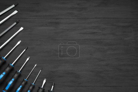Set of screwdrivers on black wooden table, top view. Space for text