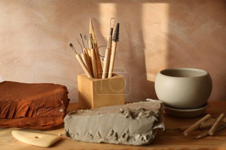Clay and set of modeling tools on wooden table in workshop
