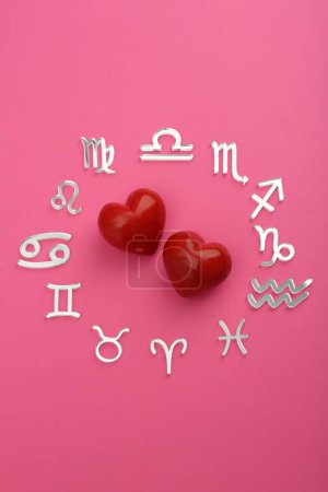 Zodiac signs and red hearts on pink background, flat lay