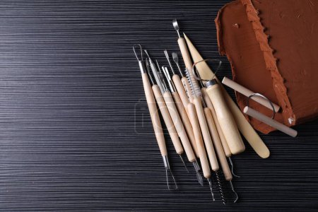 Clay and set of modeling tools on dark gray wooden table, flat lay. Space for text
