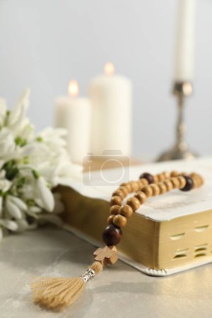 Bible, rosary beads, flowers and church candles on light table