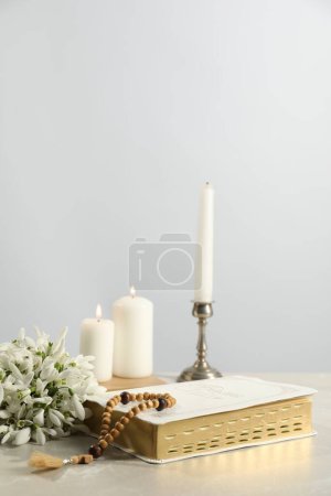 Photo for Church candles, wooden cross, rosary beads, Bible and flowers on light table - Royalty Free Image