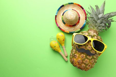 Téléchargez les photos : Chapeau sombrero mexicain, ananas avec lunettes de soleil, fausse moustache et maracas sur fond vert, plat. Espace pour le texte - en image libre de droit