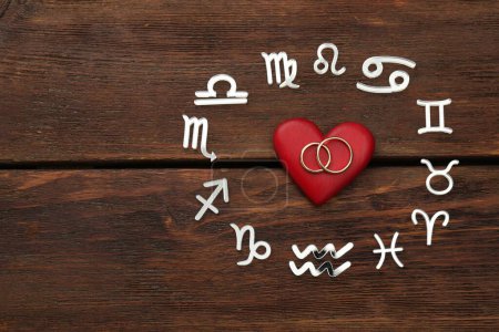 Foto de Signos del zodíaco, corazón rojo y anillos de boda sobre fondo de madera, disposición plana. Espacio para texto - Imagen libre de derechos