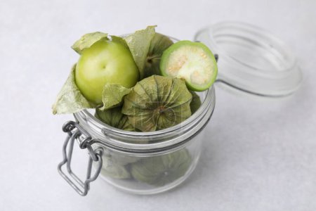 Tomates verdes frescos con cáscara en frasco de vidrio sobre mesa ligera, primer plano