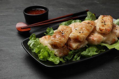 Tasty fried spring rolls, lettuce and sauce on black table, closeup