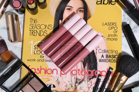 Foto de Brillante brillo labial entre diferentes productos cosméticos y revista de moda en la mesa, la puesta plana - Imagen libre de derechos