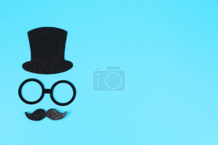 Téléchargez les photos : Visage d'homme fait de fausse moustache, chapeau et lunettes sur fond bleu clair, vue de dessus. Espace pour le texte - en image libre de droit