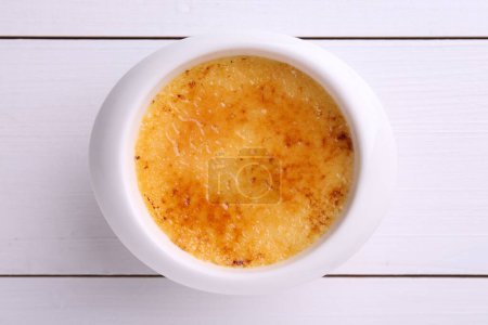 Photo for Delicious creme brulee in bowl on white wooden table, top view - Royalty Free Image