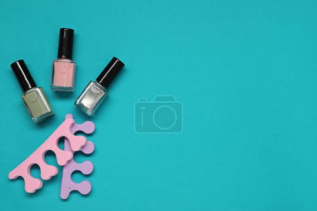 Nail polishes and separators on turquoise background, flat lay. Space for text