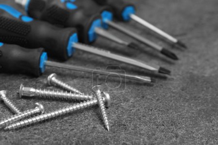Set of screwdrivers and screws on grey table, closeup