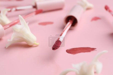 Foto de Brillos labiales de color, aplicadores y flores sobre fondo rosa, primer plano - Imagen libre de derechos