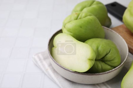 Photo for Cut and whole chayote in bowl on white tiled table, closeup. Space for text - Royalty Free Image
