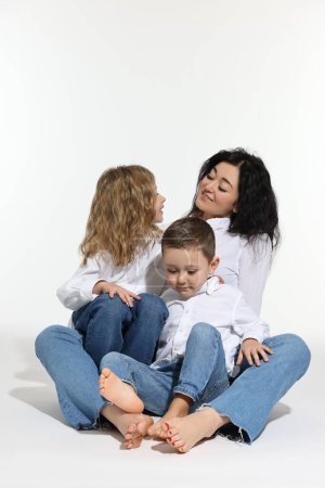 Kleine Kinder mit ihrer Mutter sitzen zusammen auf weißem Hintergrund