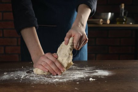 Making bread. Woman kneading dough at wooden table in kitchen, closeup