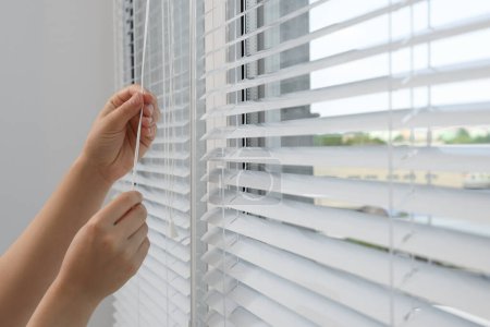 Foto de Woman opening horizontal blinds on window indoors, closeup - Imagen libre de derechos