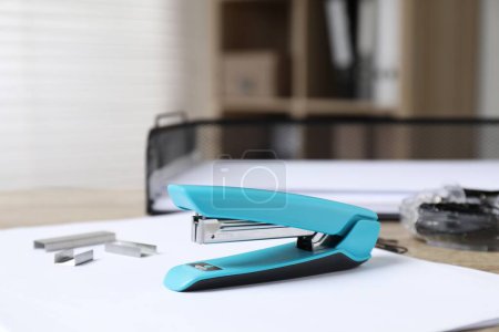 Stapler, paper and metal staples on table indoors, closeup