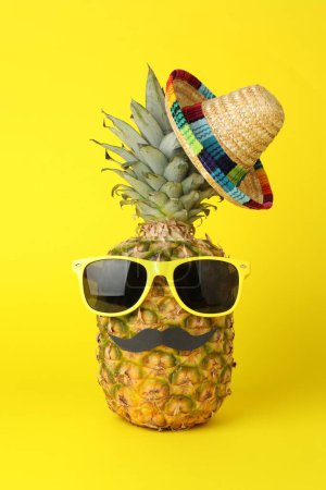 Téléchargez les photos : Ananas avec chapeau de sombrero mexicain, lunettes de soleil et fausse moustache sur fond jaune - en image libre de droit