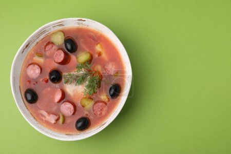 Téléchargez les photos : Soupe de viande solyanka avec de fines saucisses fumées sèches dans un bol sur fond vert clair, vue sur le dessus. Espace pour le texte - en image libre de droit