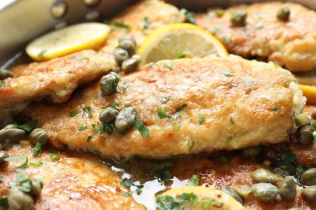 Delicious chicken piccata with herbs and lemons as background, closeup