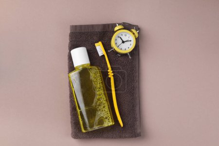 Foto de Enjuague bucal fresco en botella, cepillo de dientes, despertador y toalla sobre fondo beige, vista superior - Imagen libre de derechos