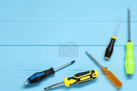 Group of different screwdrivers on light blue wooden table, top view