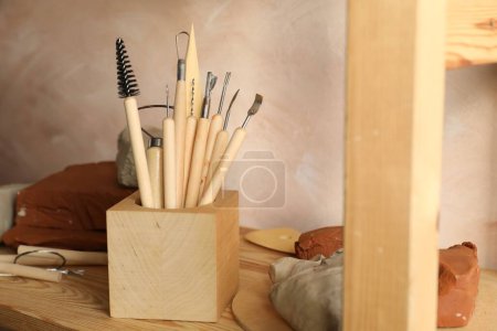 Clay and set of modeling tools on wooden table in workshop