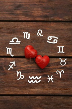 Zodiac signs and red hearts on wooden background, flat lay