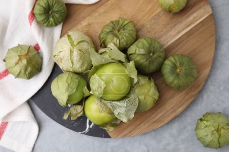 Tomates verdes frescos con cáscara sobre mesa gris, puesta plana