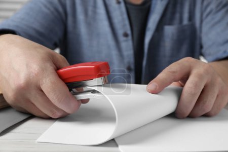 Man with papers using stapler at white wooden table, closeup