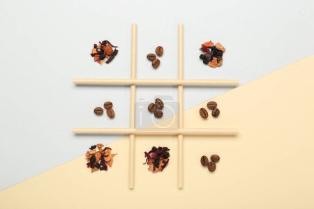 Tic Tac Toe Spiel mit Kaffeebohnen und trockenen Teeblättern auf farbigem Hintergrund, Ansicht von oben