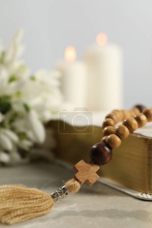 Photo for Bible, rosary beads and church candles on light table, closeup - Royalty Free Image
