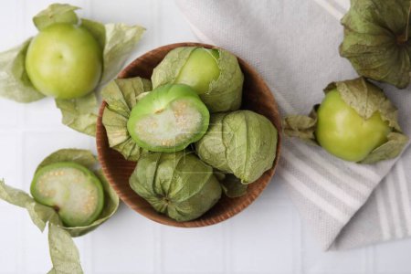 Fresh green tomatillos with husk in bowl on white table, flat lay