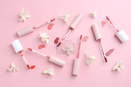Foto de Diferentes brillos labiales, aplicadores y flores sobre fondo rosa, disposición plana - Imagen libre de derechos