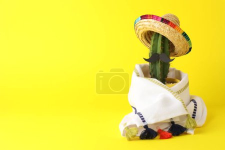 Téléchargez les photos : Cactus avec chapeau de sombrero mexicain, fausse moustache et poncho sur fond jaune, espace pour le texte - en image libre de droit