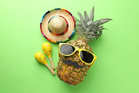 Téléchargez les photos : Chapeau sombrero mexicain, ananas avec lunettes de soleil, fausse moustache et maracas sur fond vert, plat - en image libre de droit