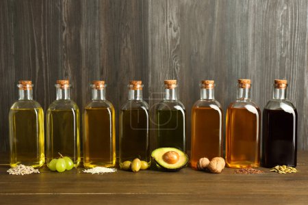 Foto de Grasas vegetales. Diferentes aceites en botellas de vidrio e ingredientes en mesa de madera - Imagen libre de derechos