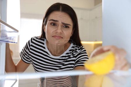 Mujer molesta cerca de refrigerador vacío en la cocina, vista desde el interior