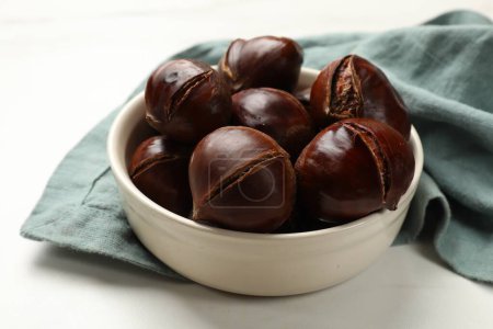 Roasted edible sweet chestnuts in bowl on white table, closeup