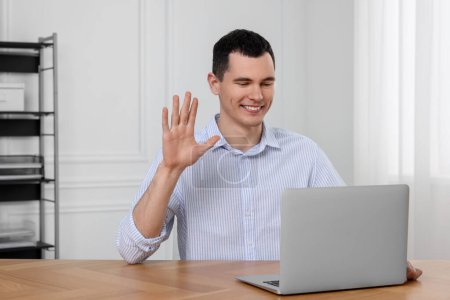 Foto de Hombre saludando mientras tiene chat de vídeo en el ordenador portátil en la oficina - Imagen libre de derechos