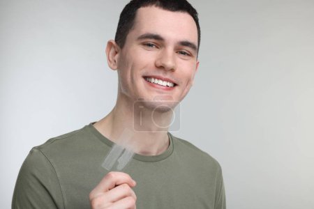Young man with whitening strips on light grey background