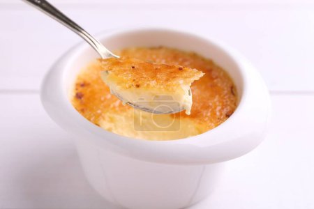 Photo for Taking delicious creme brulee with spoon from bowl at white table, closeup - Royalty Free Image