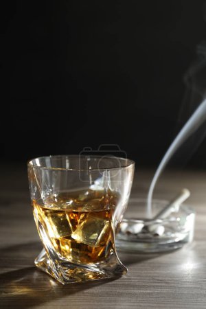Téléchargez les photos : L'alcoolisme. Whisky en verre, cigarettes et cendrier sur table en bois - en image libre de droit