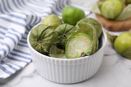 Tomatillos verts frais avec enveloppe dans un bol sur une table en marbre clair, gros plan