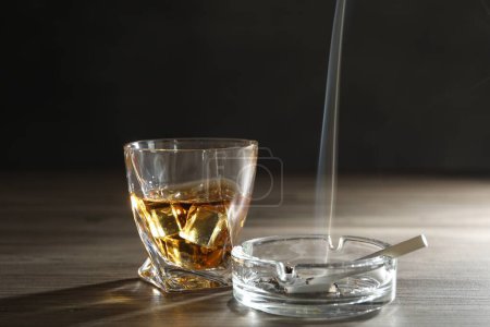 Adicción al alcohol. Whisky en vidrio, cigarrillos y cenicero sobre mesa de madera