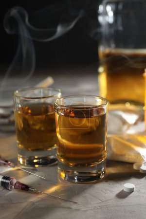 Foto de Alcohol y drogadicción. Whisky en vasos, jeringas y pastillas sobre fondo gris - Imagen libre de derechos