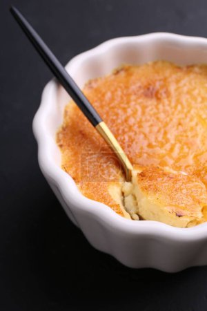 Photo for Delicious creme brulee in bowl and spoon on dark gray table, closeup - Royalty Free Image
