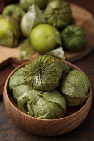 Fresh green tomatillos with husk in bowl on wooden table, closeup
