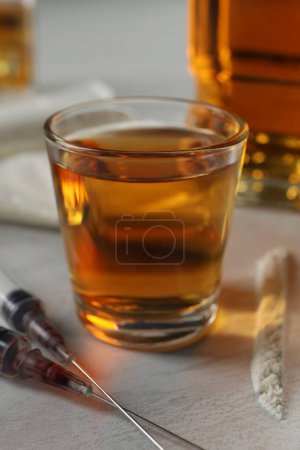 Téléchargez les photos : Alcool et toxicomanie. Whisky en verre, seringues et cocaïne sur table blanche, gros plan - en image libre de droit